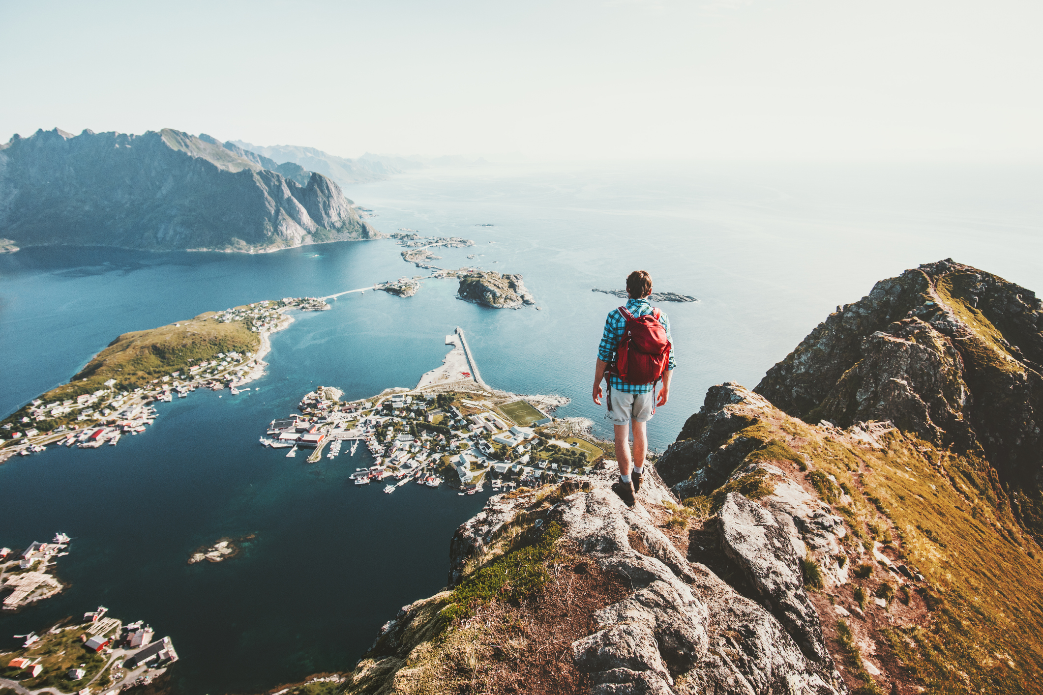 Man traveler hiking on Reinebringen mountain ridge in Norway lifestyle adventure traveling outdoor summer vacations enjoying aerial view Lofoten islands